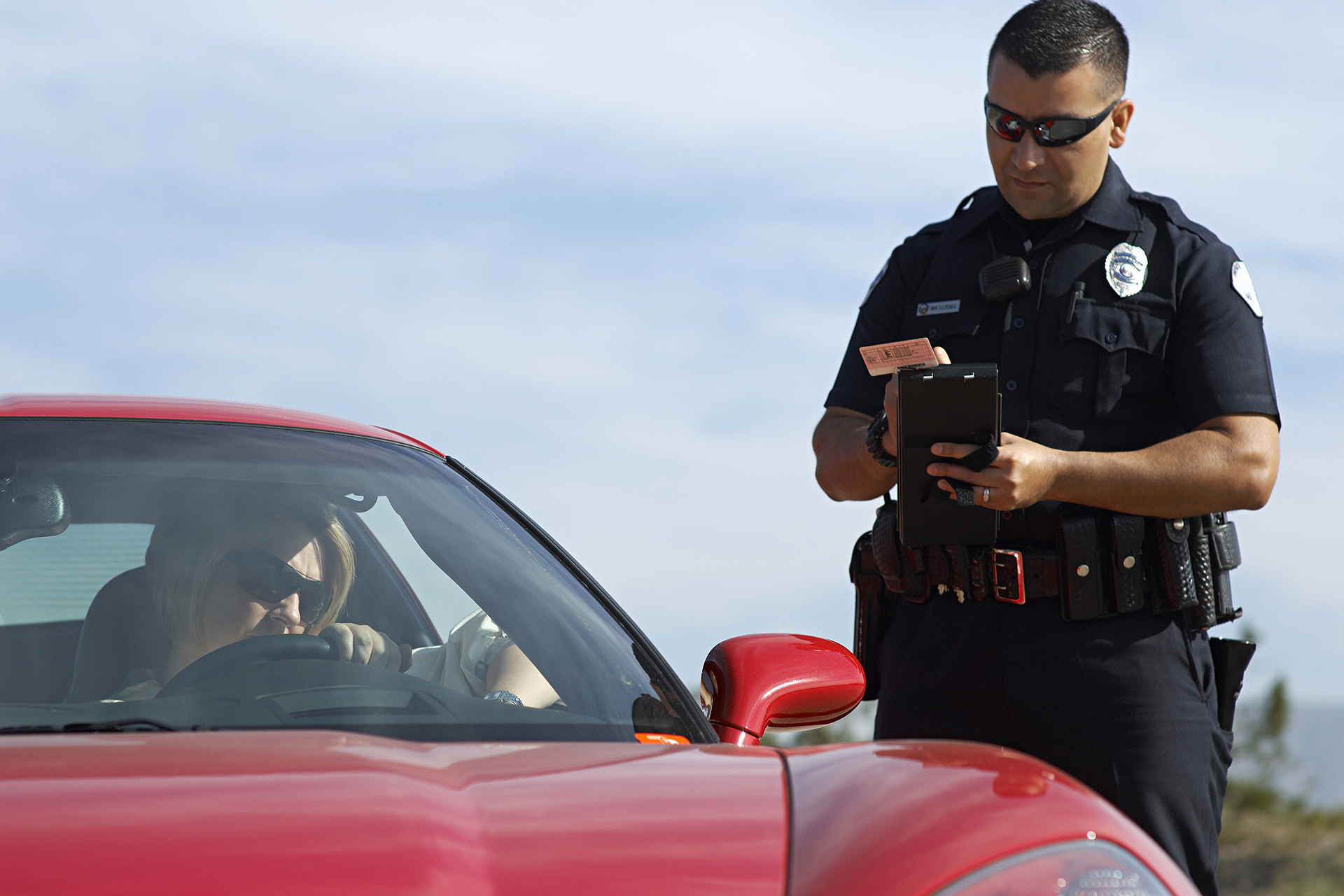 Police Officer Issuing Traffic Ticket to Woman In Red Sports Car